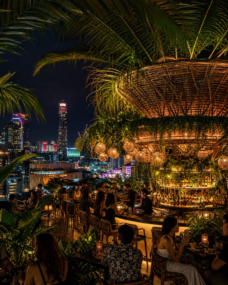A lush tropical rooftop bar lit by lanterns over the city at night